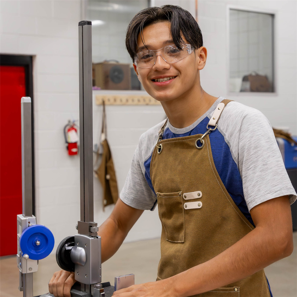 Manufacturing student looks at camera standing at equipment